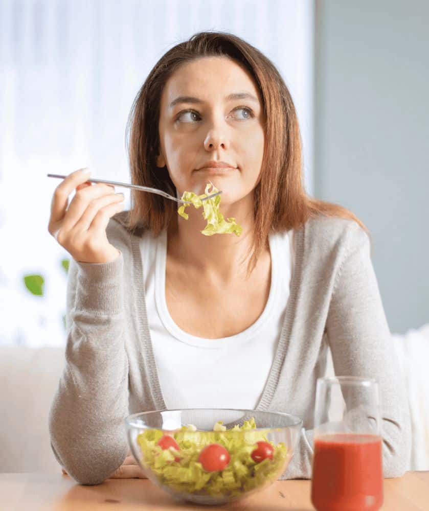 Woman eating salad while looking thoughtful